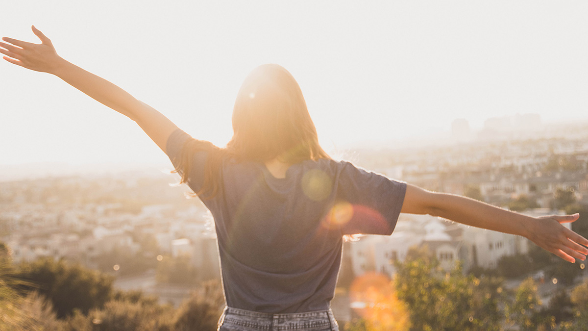 student with arms stretched out looking at the sun